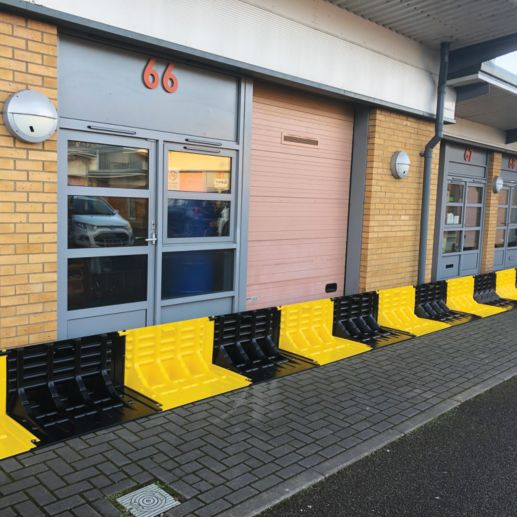 Yellow and black flood fence barrier running along a building with doors