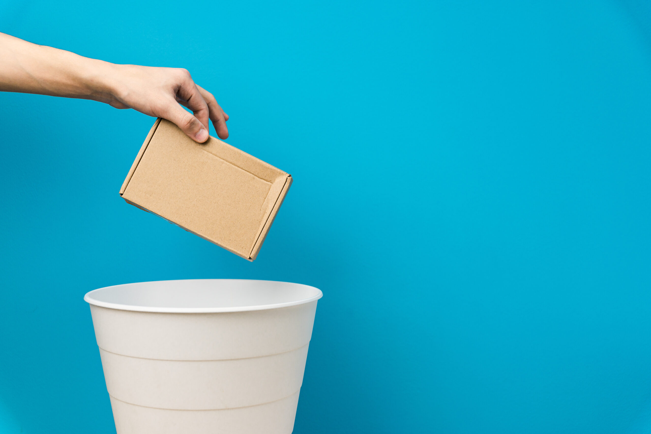 Hand throwing a cardboard box in a bin